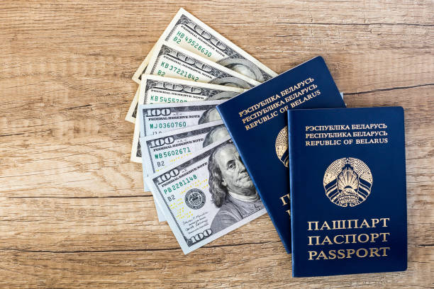 Passports on a wooden background with a fan of dollars Two Belarusian passports on a brown wooden background with a fan of American dollars. Travel, help and immigration concept Visa-Free Countries That Are Budget Friendly stock pictures, royalty-free photos & images
