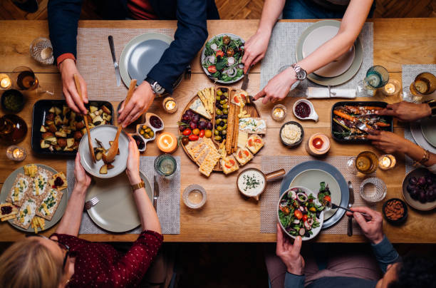 Unrecognizable Friends And Family Sharing Food At Dinning Room From above photo of group of friends enjoys eating delicious vegetarian food during a dinner celebration. Sharing food is fun stock pictures, royalty-free photos & images