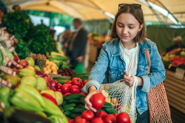 Young girl choosing vegetables and fruit at a farmers market with reusable bag, plastic free and zero waste concept Teenager holding ecologically friendly reusable bag with fruit and vegetables Shop at the local market stock pictures, royalty-free photos & images