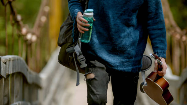 Young man with a backpack, guitar and bottle of water walking on the bridge Young man with a backpack, guitar and bottle of water walking on the bridge. Mid shot Utilize a water bottle for travel stock pictures, royalty-free photos & images